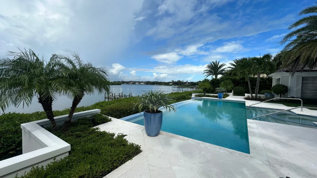 Waterfront residential landscape with palms, clipped hedges and planted containers around a pool