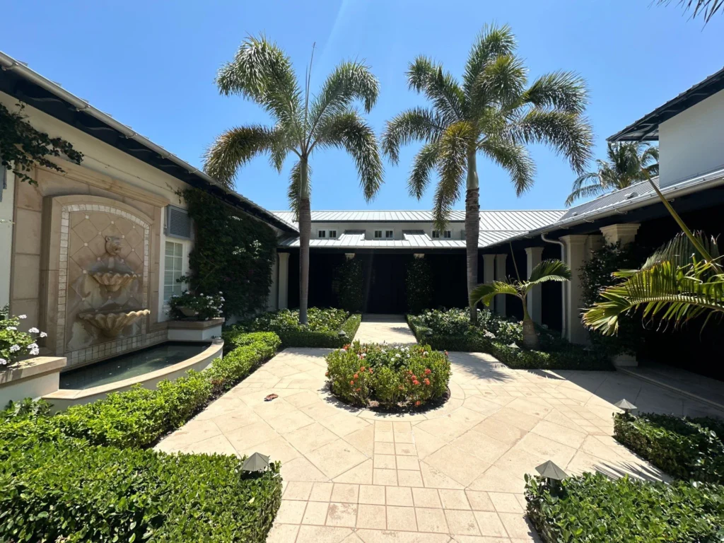 Palm-lined courtyard with flowering garden beds and clipped hedges along a paved walkway